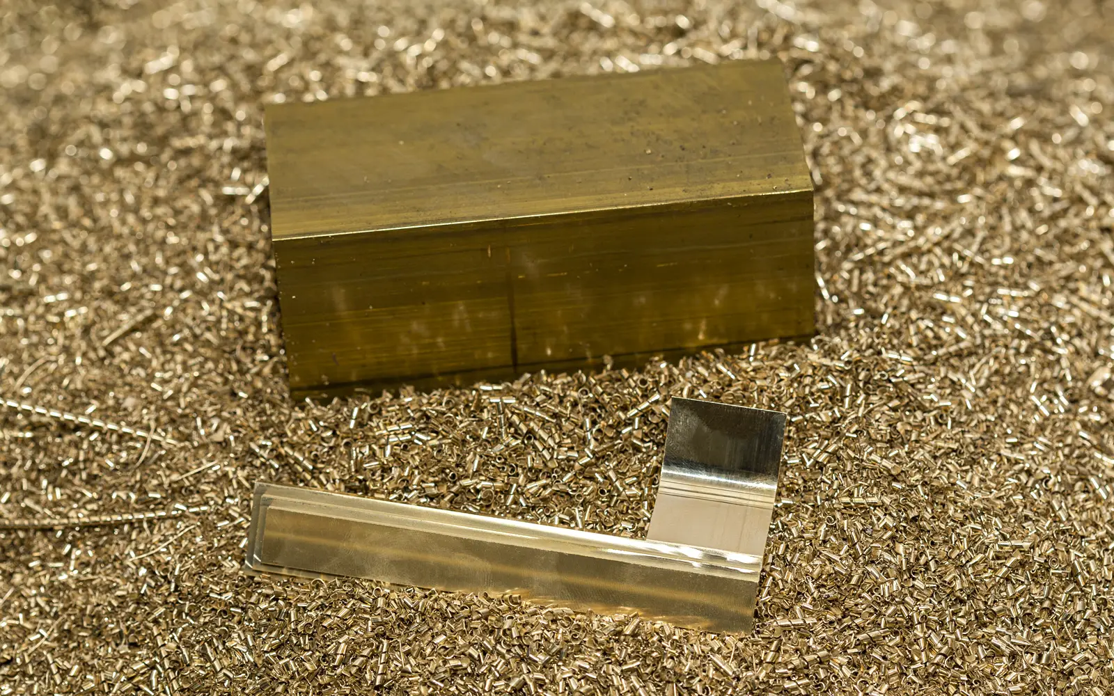 A solid block of brass and a lever handle placed on brass shavings.